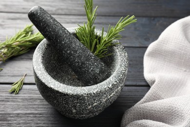 Photo of Stone mortar with rosemary and pestle on black wooden table, closeup