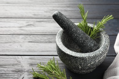 Photo of Stone mortar with rosemary and pestle on black wooden table, closeup. Space for text