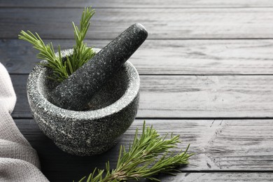 Photo of Stone mortar with rosemary and pestle on black wooden table, closeup. Space for text