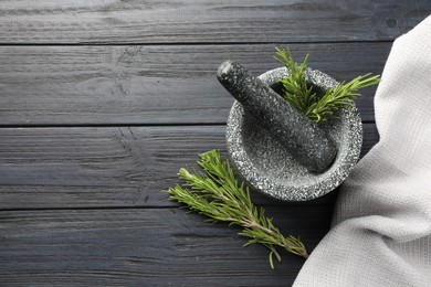 Photo of Stone mortar with rosemary and pestle on black wooden table, flat lay. Space for text