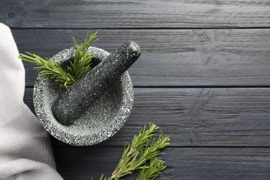 Photo of Stone mortar with rosemary and pestle on black wooden table, flat lay. Space for text