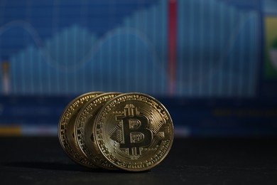 Photo of Cryptocurrency. Three bitcoins on black table against data charts, closeup