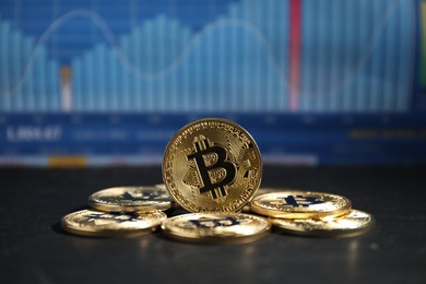 Photo of Cryptocurrency. Bitcoins on black table against data charts, closeup