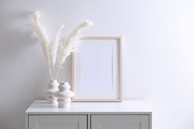 Photo of Empty picture frame and stylish home decor on cabinet near white wall indoors