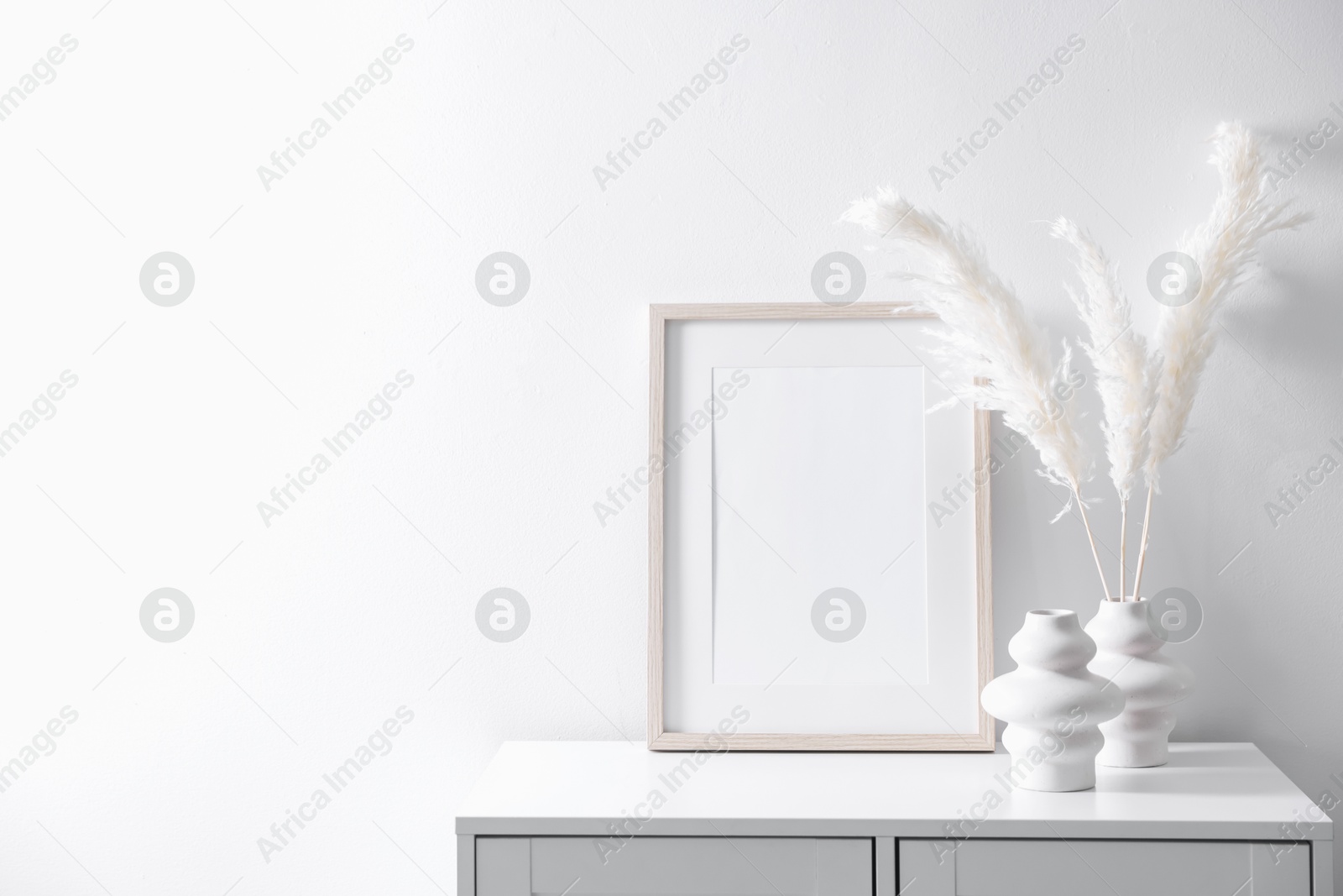 Empty picture frame and stylish home decor on cabinet near white wall indoors Photo of Empty picture frame and stylish home decor on cabinet near white wall indoors