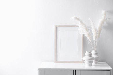 Photo of Empty picture frame and stylish home decor on cabinet near white wall indoors