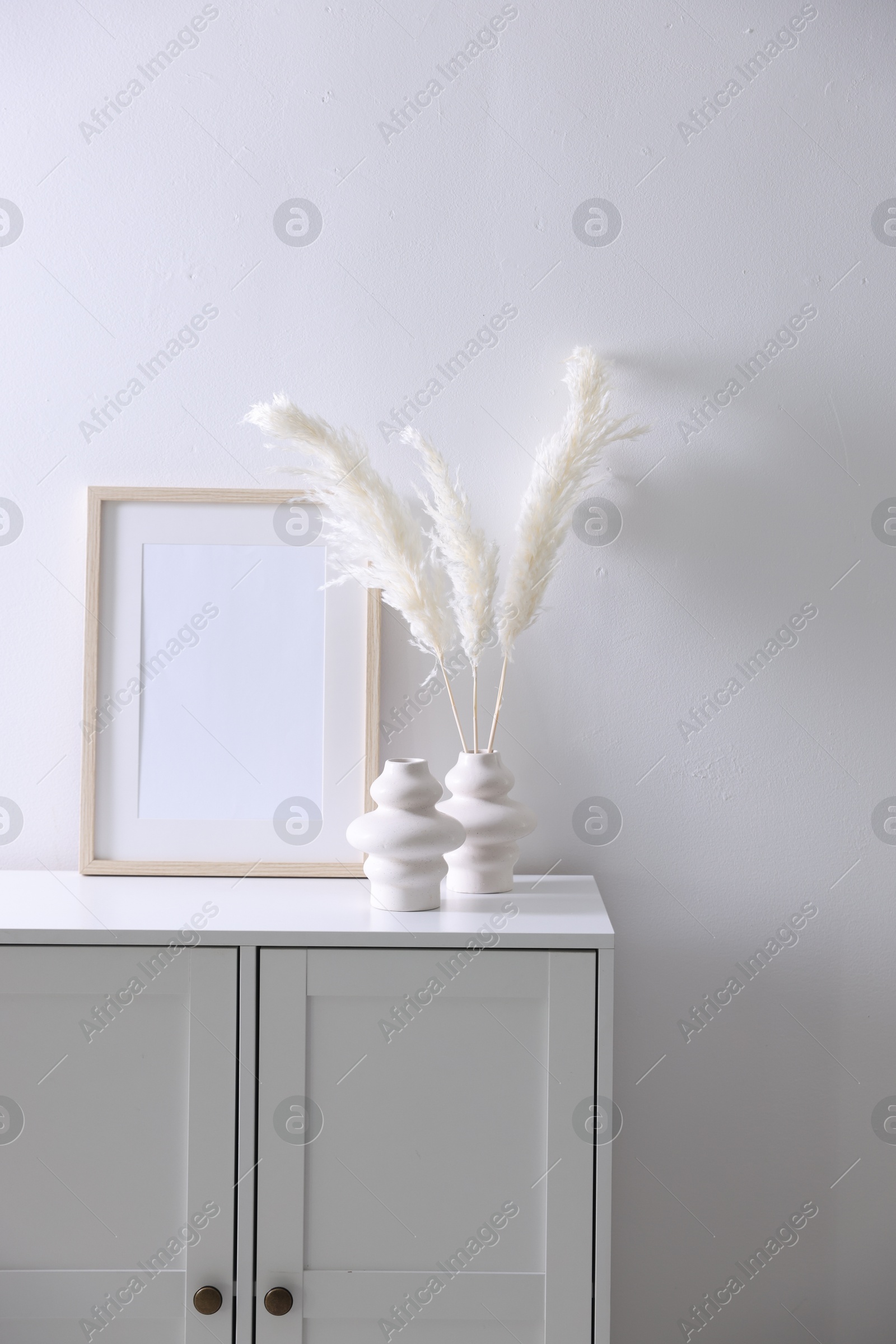 Empty picture frame and stylish home decor on cabinet near white wall indoors Photo of Empty picture frame and stylish home decor on cabinet near white wall indoors