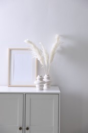 Photo of Empty picture frame and stylish home decor on cabinet near white wall indoors