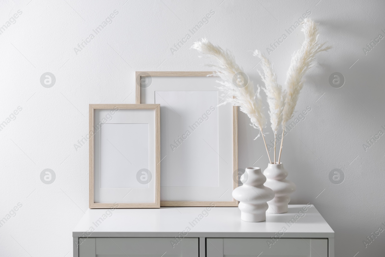 Empty picture frames and stylish home decor on cabinet near white wall indoors Photo of Empty picture frames and stylish home decor on cabinet near white wall indoors