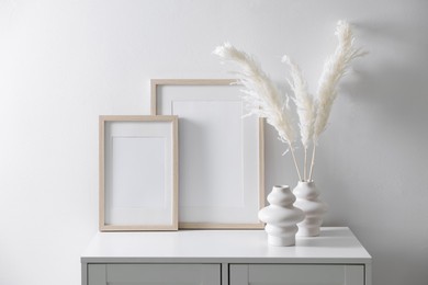 Photo of Empty picture frames and stylish home decor on cabinet near white wall indoors