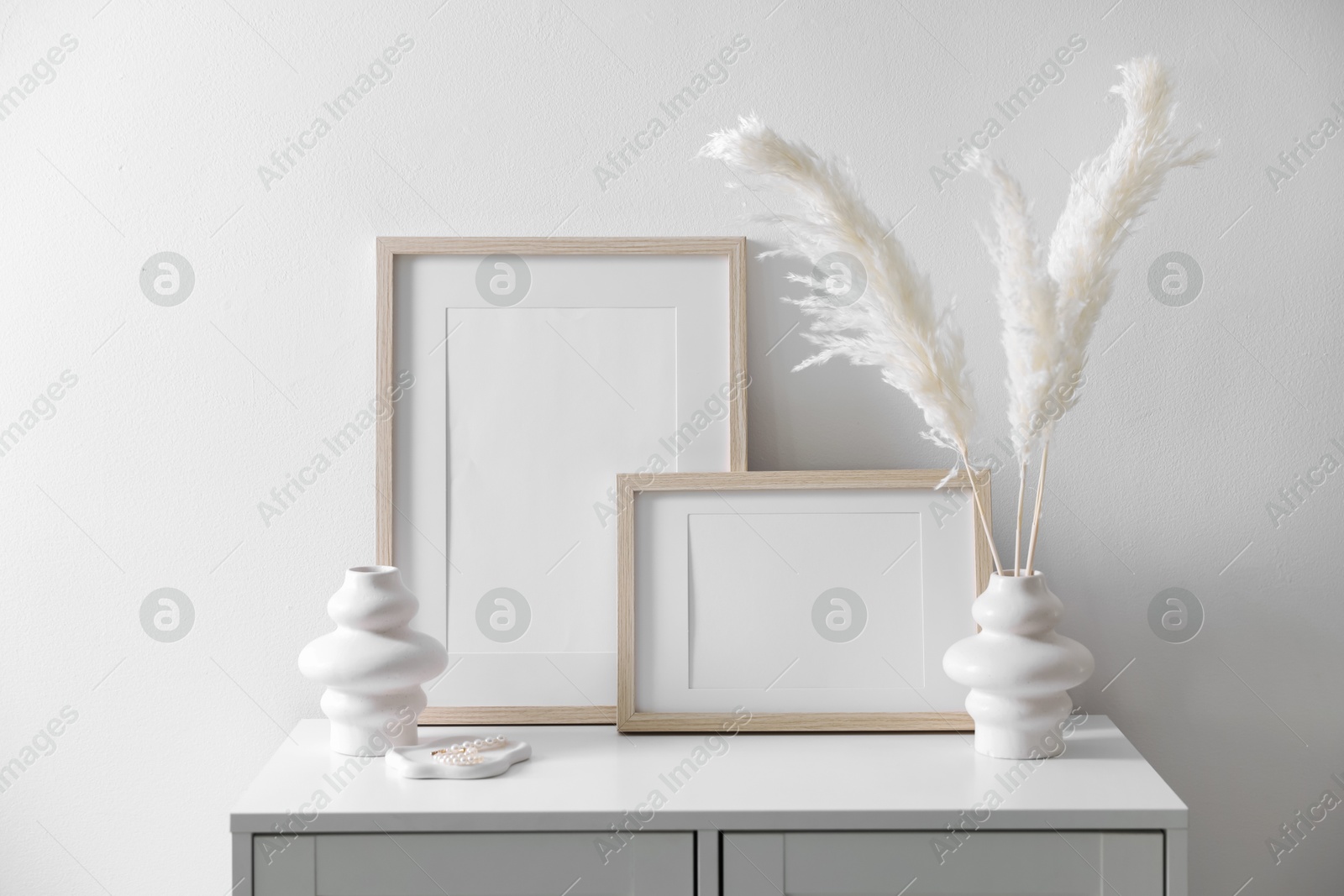 Empty picture frames and stylish home decor on cabinet near white wall indoors Photo of Empty picture frames and stylish home decor on cabinet near white wall indoors