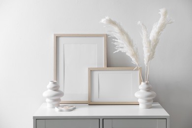 Photo of Empty picture frames and stylish home decor on cabinet near white wall indoors