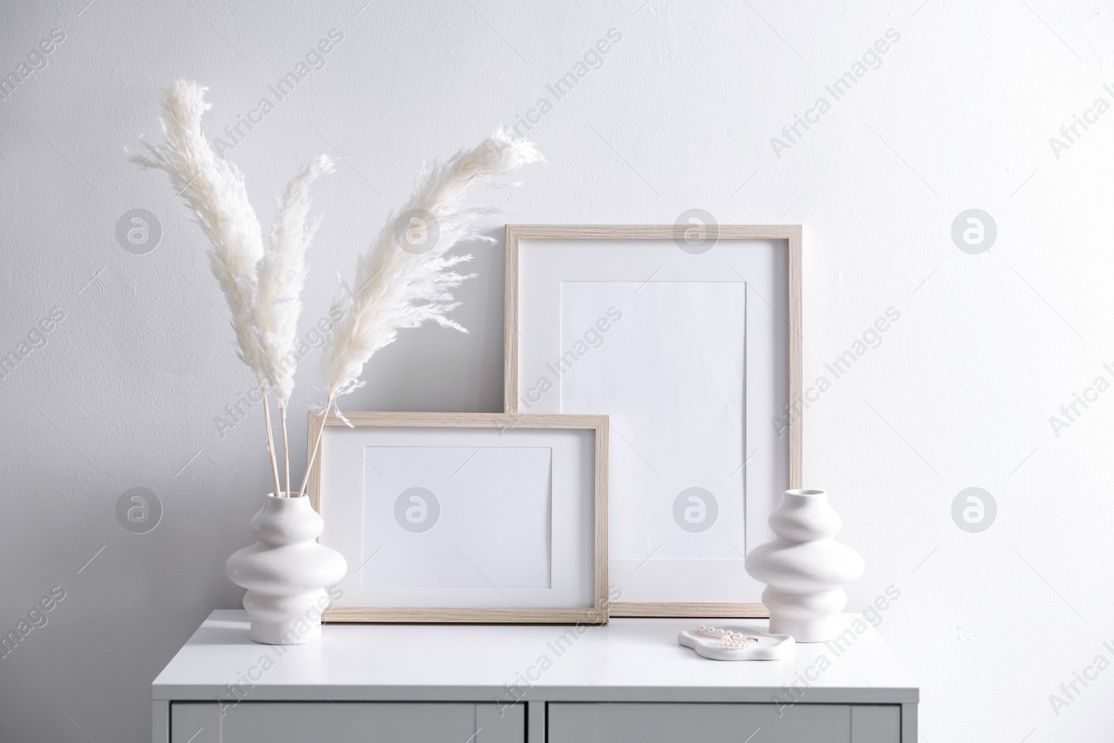Empty picture frames and stylish home decor on cabinet near white wall indoors Photo of Empty picture frames and stylish home decor on cabinet near white wall indoors