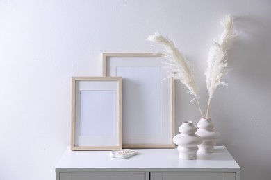 Photo of Empty picture frames and stylish home decor on cabinet near white wall indoors