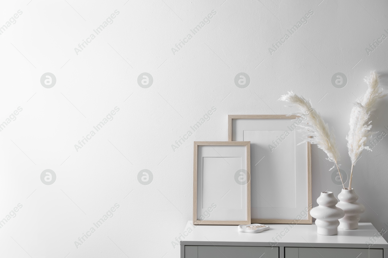Empty picture frames and stylish home decor on cabinet near white wall indoors, space for text Photo of Empty picture frames and stylish home decor on cabinet near white wall indoors, space for text