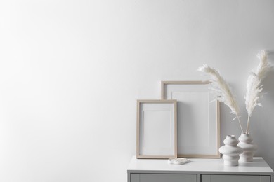 Photo of Empty picture frames and stylish home decor on cabinet near white wall indoors, space for text