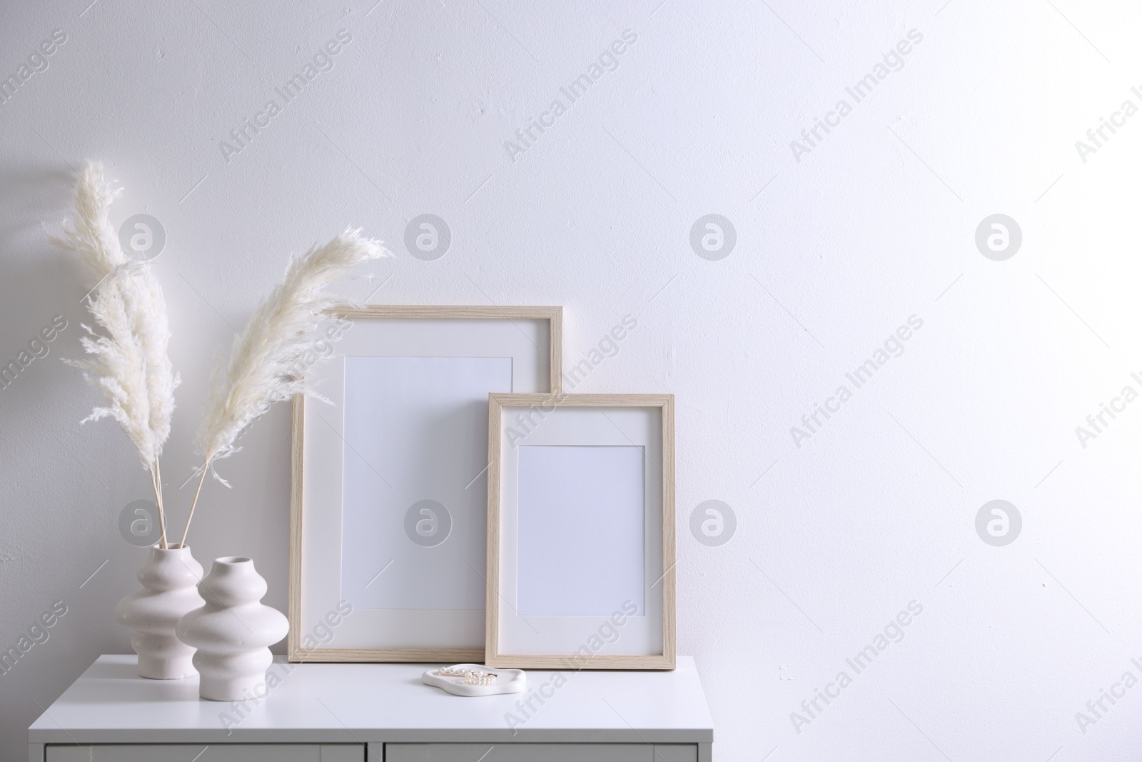 Empty picture frames and stylish home decor on cabinet near white wall indoors, space for text Photo of Empty picture frames and stylish home decor on cabinet near white wall indoors, space for text