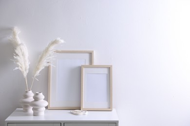 Photo of Empty picture frames and stylish home decor on cabinet near white wall indoors, space for text