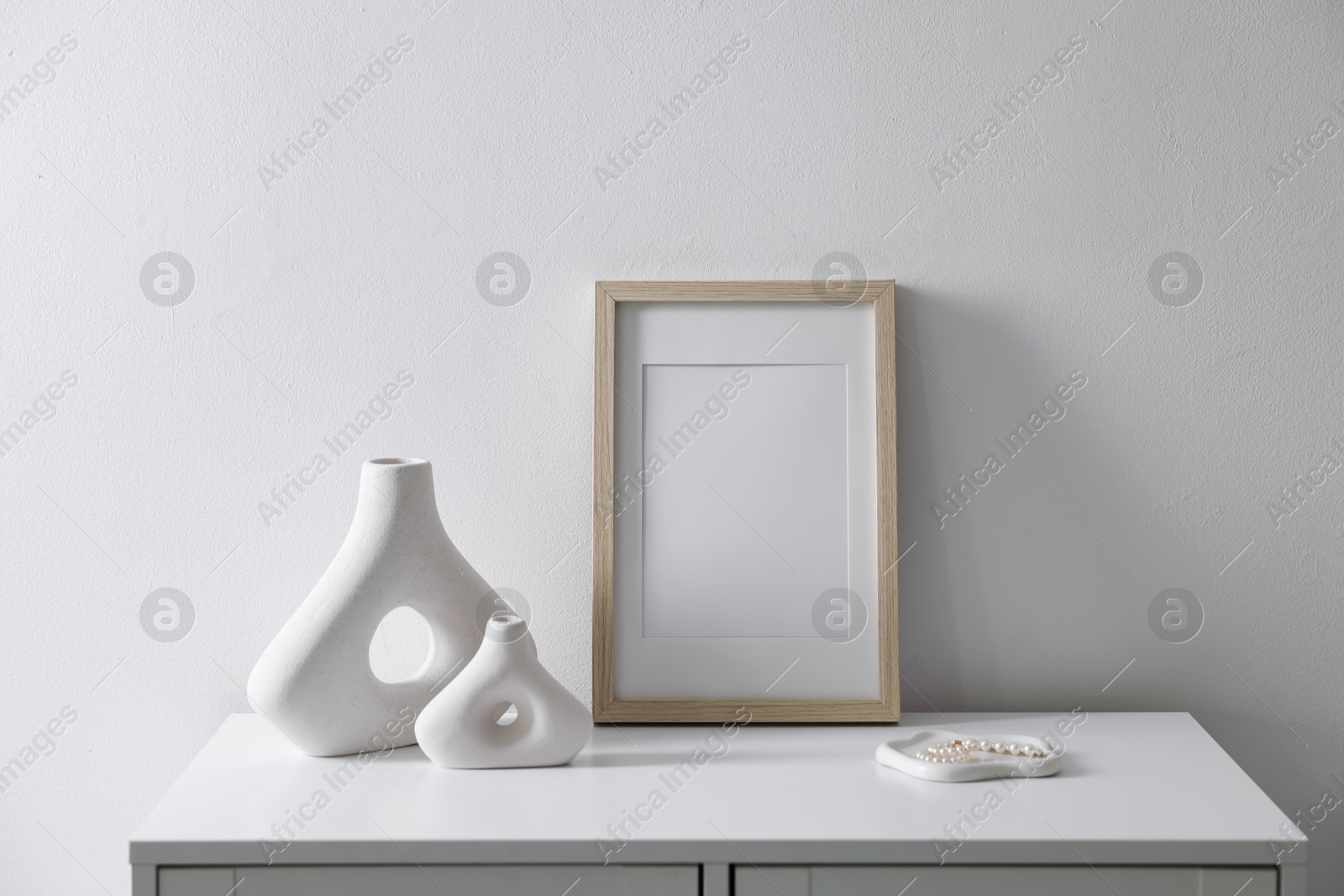 Empty picture frame and stylish home decor on cabinet near white wall indoors Photo of Empty picture frame and stylish home decor on cabinet near white wall indoors