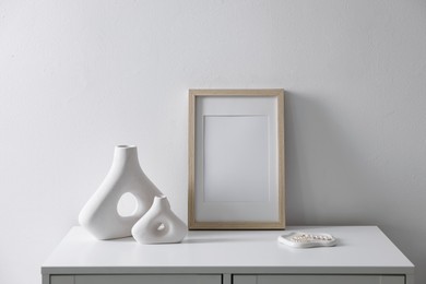 Photo of Empty picture frame and stylish home decor on cabinet near white wall indoors