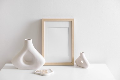 Photo of Empty picture frame and stylish home decor on cabinet near white wall indoors