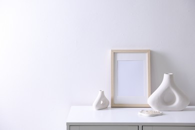 Photo of Empty picture frame and stylish home decor on cabinet near white wall indoors, space for text