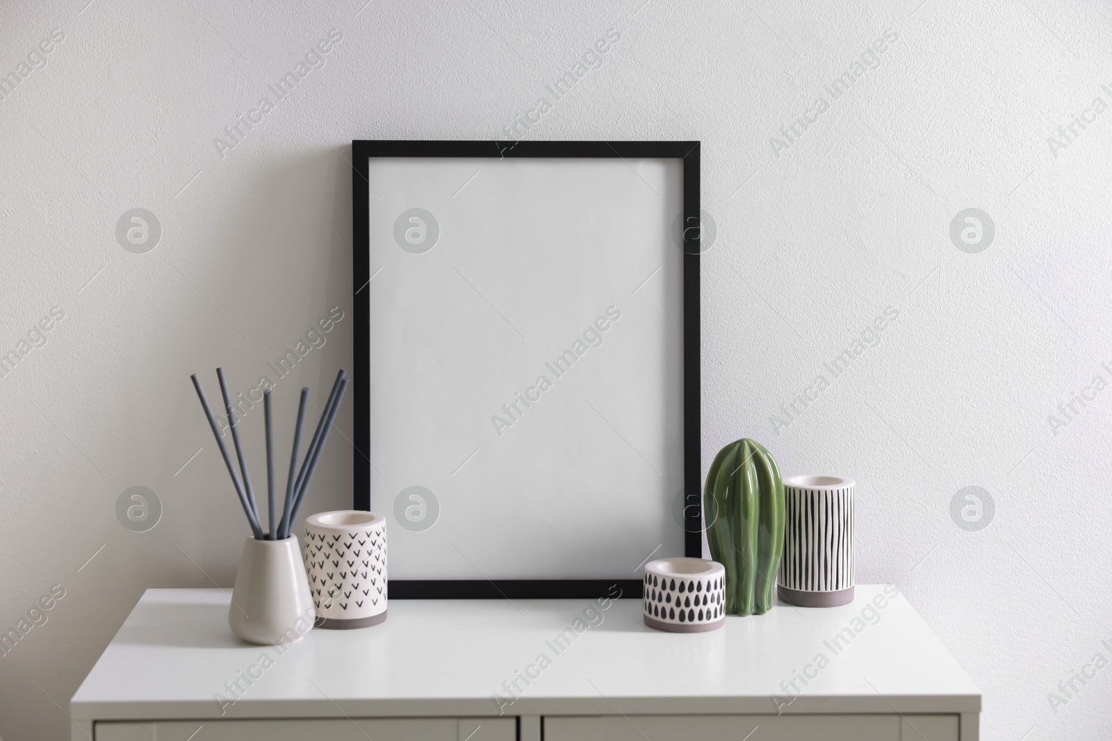 Empty picture frame, reed diffuser and stylish home decor on cabinet near white wall indoors Photo of Empty picture frame, reed diffuser and stylish home decor on cabinet near white wall indoors