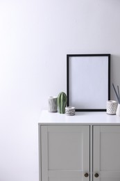 Photo of Empty picture frame, reed diffuser and stylish home decor on cabinet near white wall indoors