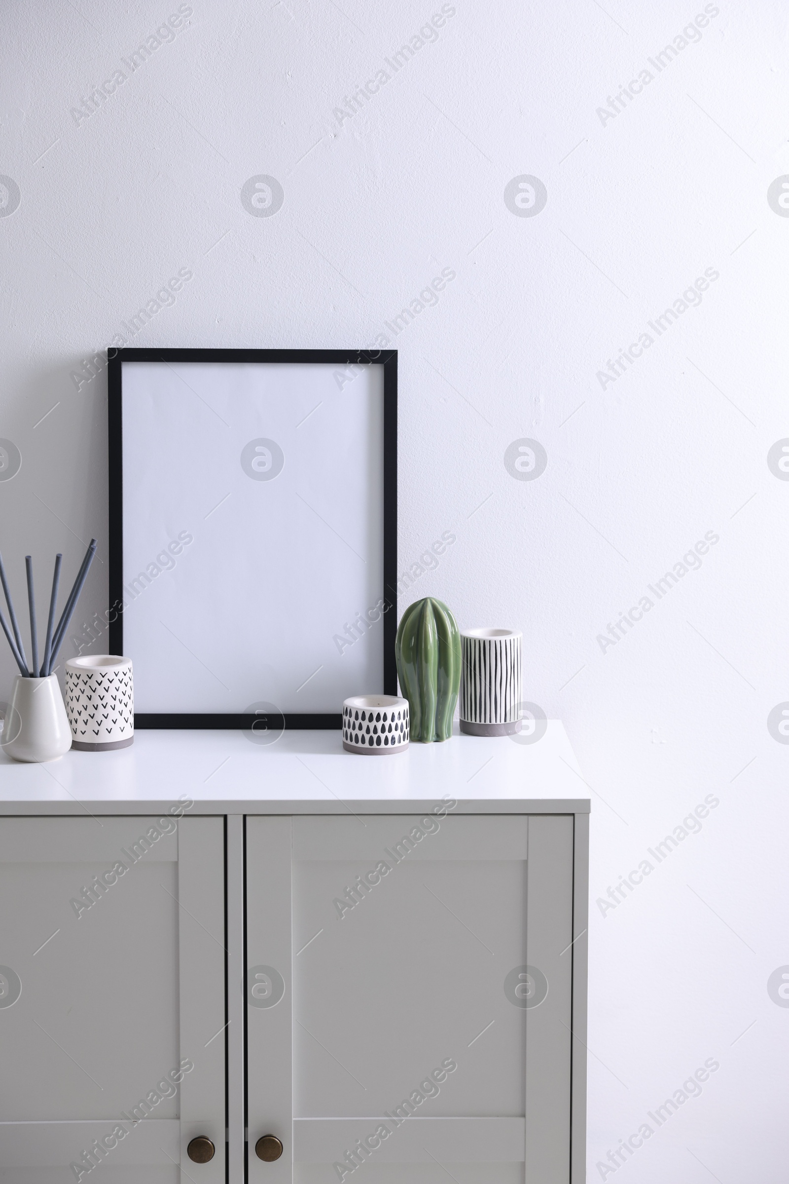 Empty picture frame, reed diffuser and stylish home decor on cabinet near white wall indoors Photo of Empty picture frame, reed diffuser and stylish home decor on cabinet near white wall indoors