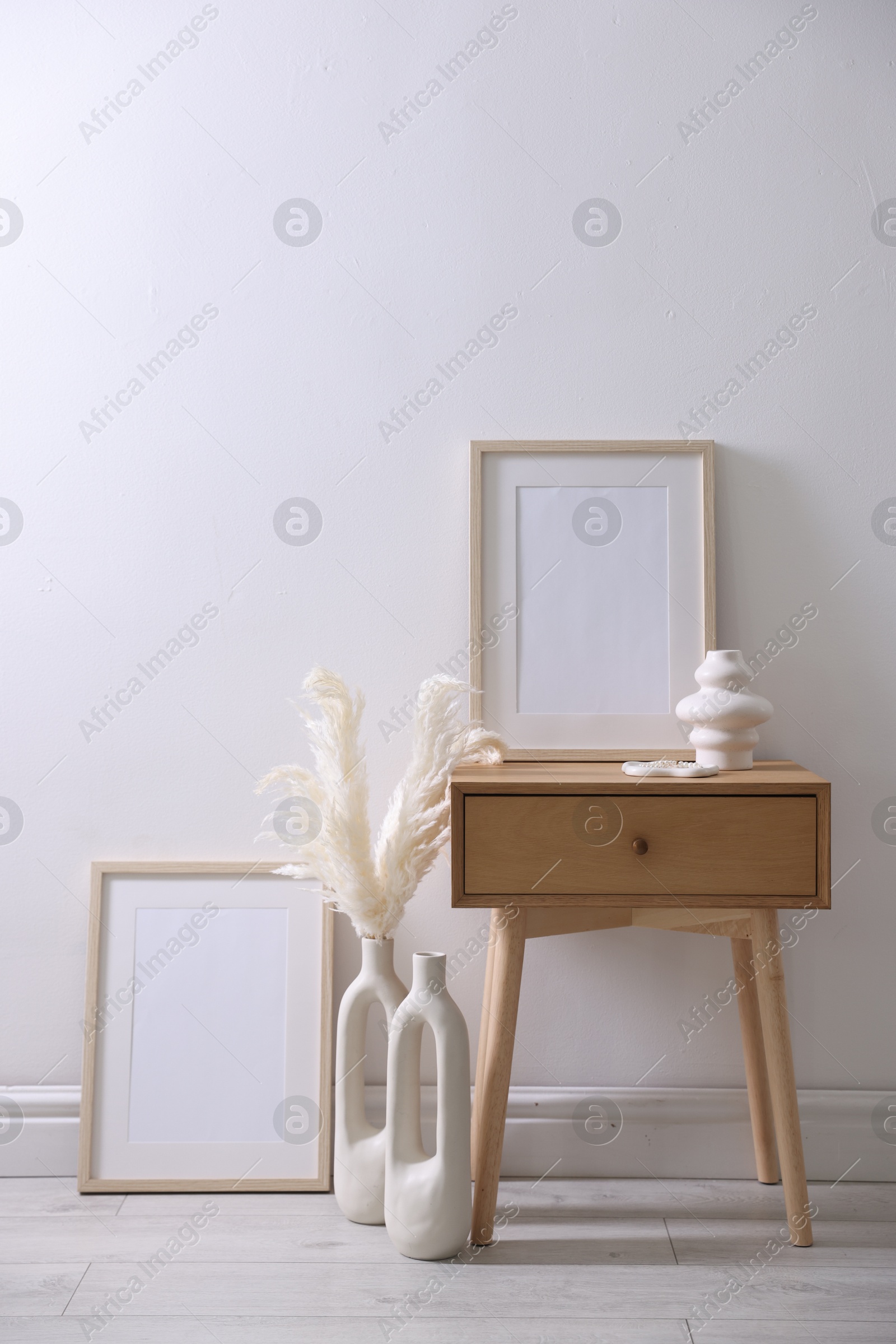 Empty picture frames, table and stylish home decor near white wall indoors Photo of Empty picture frames, table and stylish home decor near white wall indoors