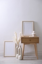 Photo of Empty picture frames, table and stylish home decor near white wall indoors