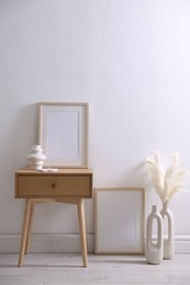 Photo of Empty picture frames, table and stylish home decor near white wall indoors