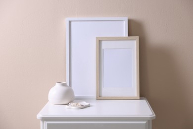 Photo of Empty picture frames, vase and jewelry on cabinet near beige wall indoors