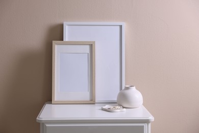 Photo of Empty picture frames, vase and jewelry on cabinet near beige wall indoors