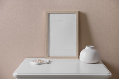 Photo of Empty picture frame, vase and jewelry on cabinet near beige wall indoors