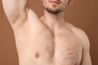 Photo of Young man showing hairy armpit on brown background, closeup. Epilation procedure