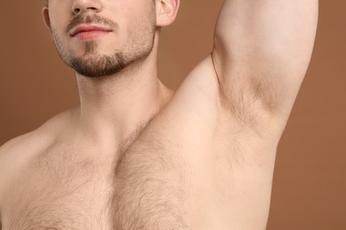 Photo of Young man showing hairy armpit on brown background, closeup. Epilation procedure