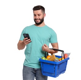 Photo of Man with shopping basket full of products using smartphone on white background