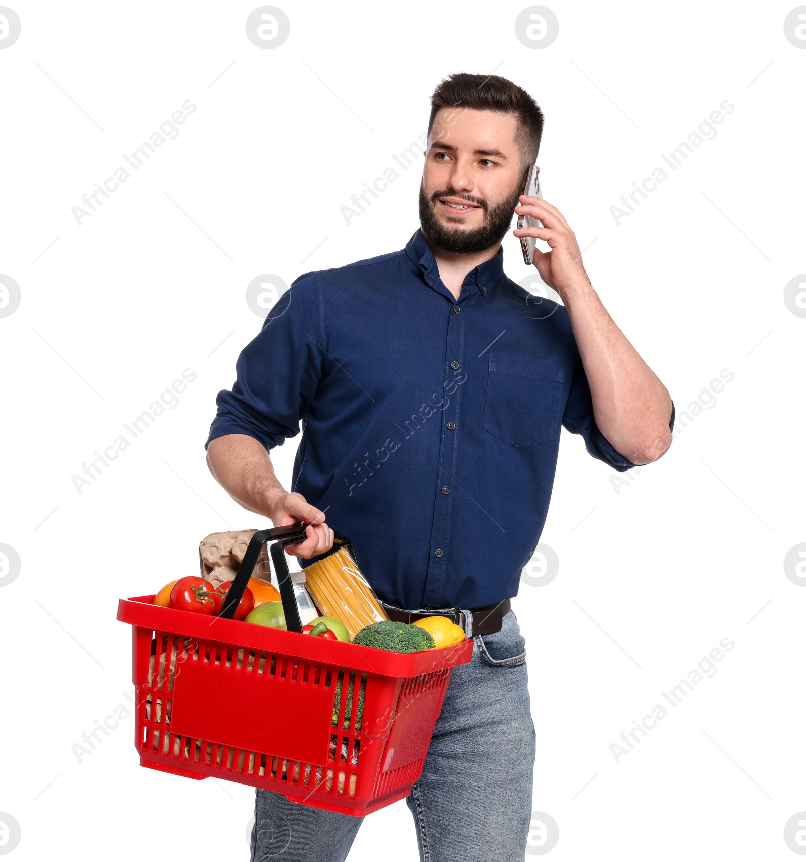 Man with shopping basket full of products talking on smartphone against white background Photo of Man with shopping basket full of products talking on smartphone against white background