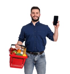 Photo of Man with shopping basket full of products and smartphone on white background