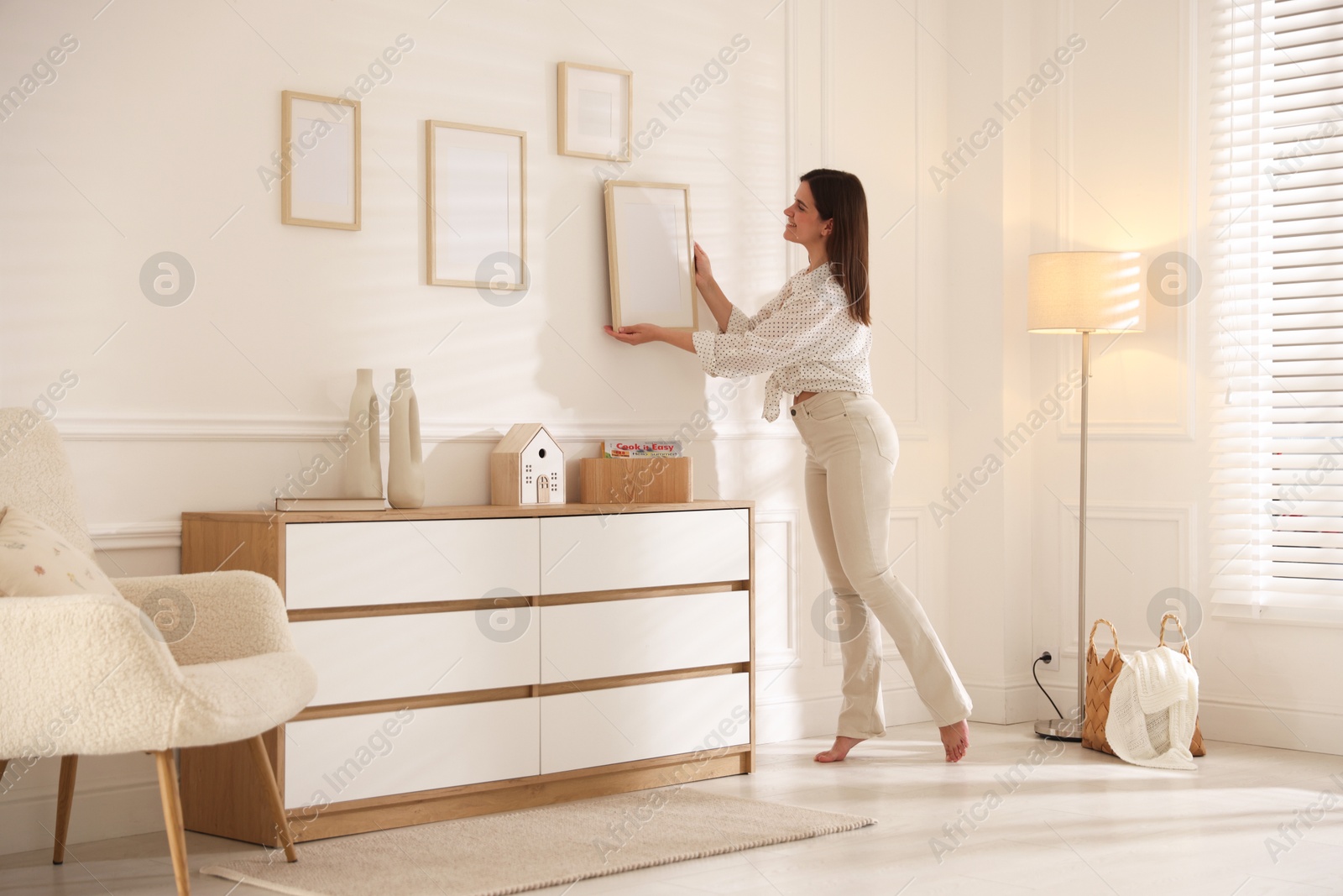 Woman hanging blank frames on white wall indoors Photo of Woman hanging blank frames on white wall indoors