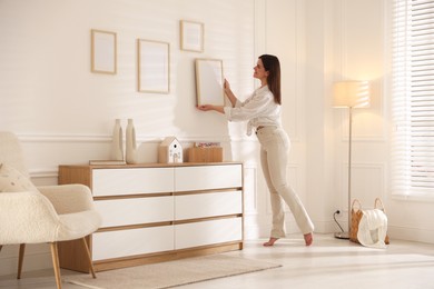 Photo of Woman hanging blank frames on white wall indoors