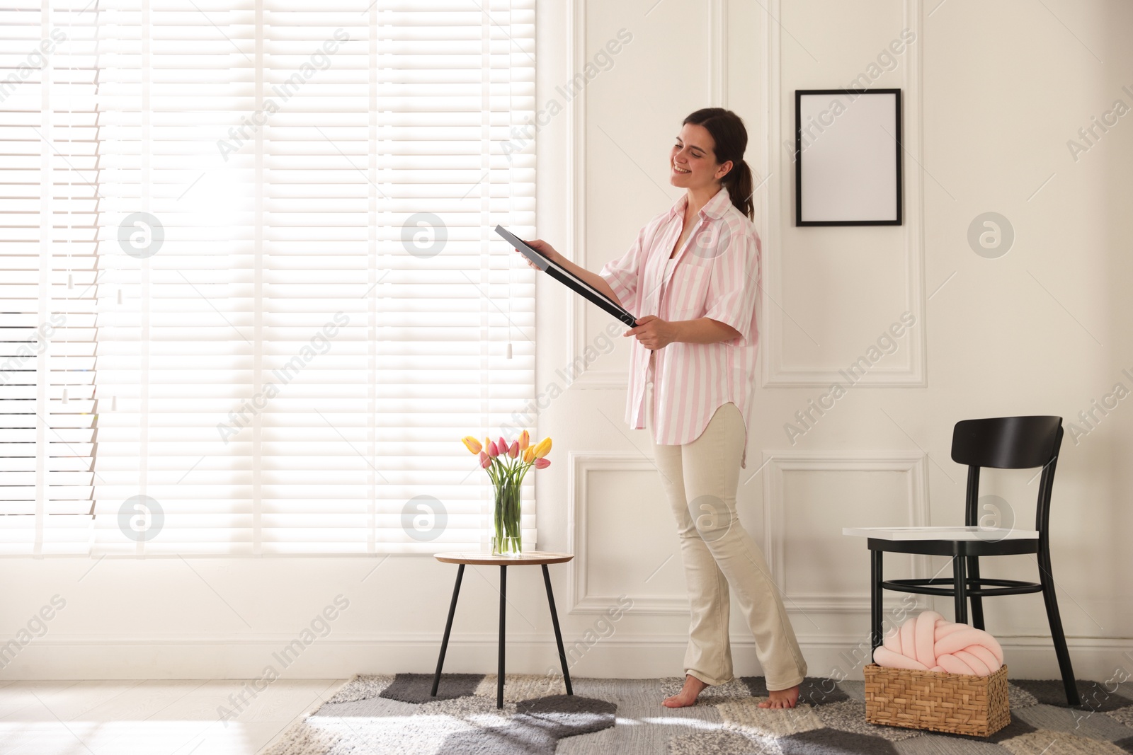Photo of Woman hanging blank frames on white wall indoors