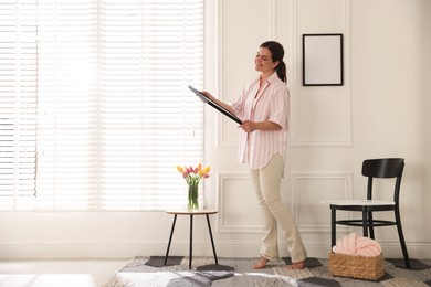 Photo of Woman hanging blank frames on white wall indoors