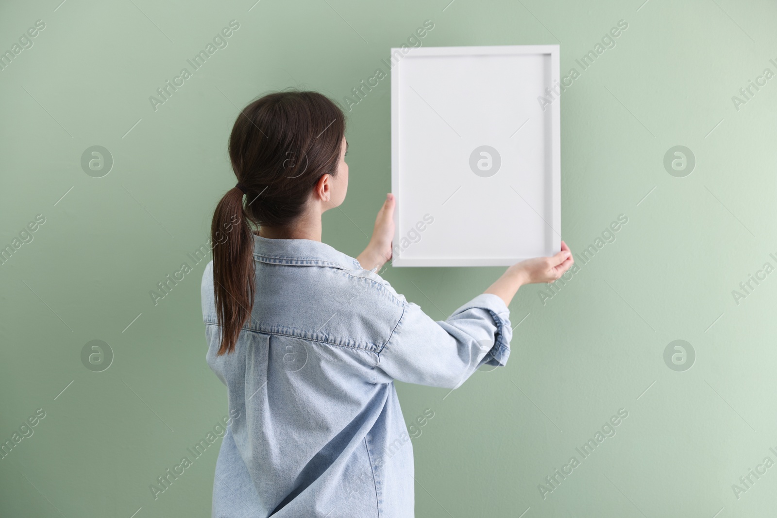 Woman hanging blank frame on green wall, back view Photo of Woman hanging blank frame on green wall, back view