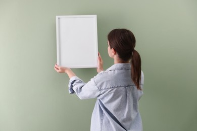 Photo of Woman hanging blank frame on green wall, back view