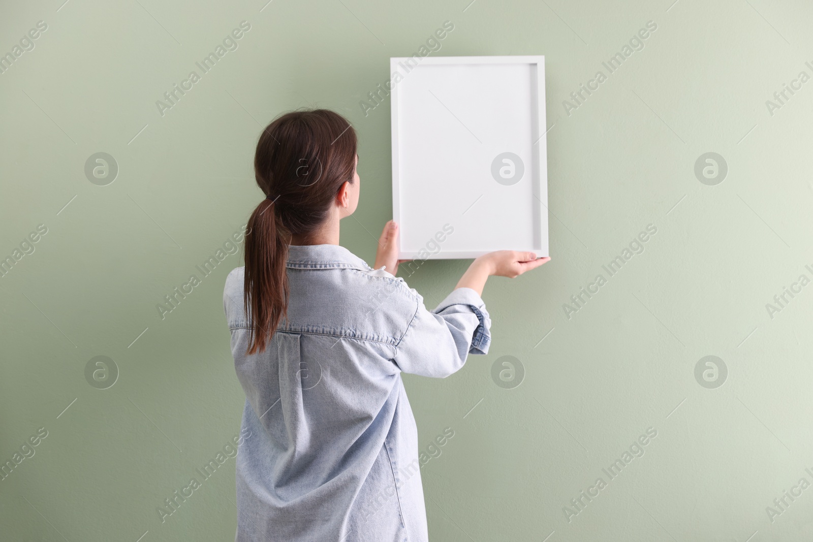 Woman hanging blank frame on green wall, back view Photo of Woman hanging blank frame on green wall, back view