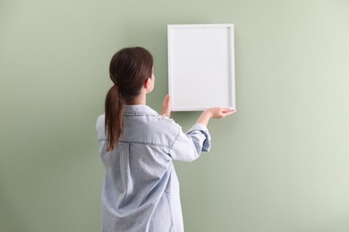 Photo of Woman hanging blank frame on green wall, back view