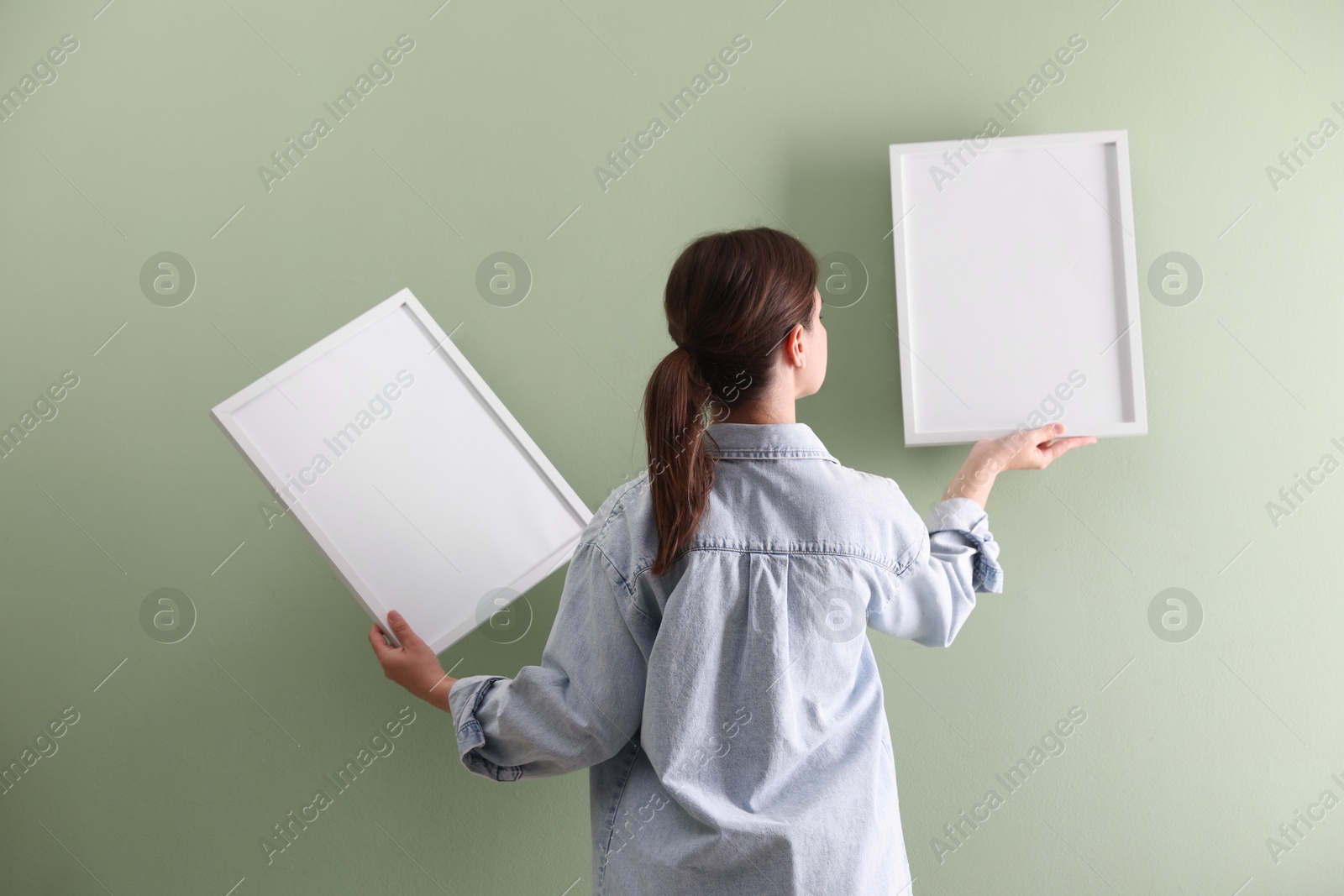 Woman hanging blank frames on green wall, back view Photo of Woman hanging blank frames on green wall, back view