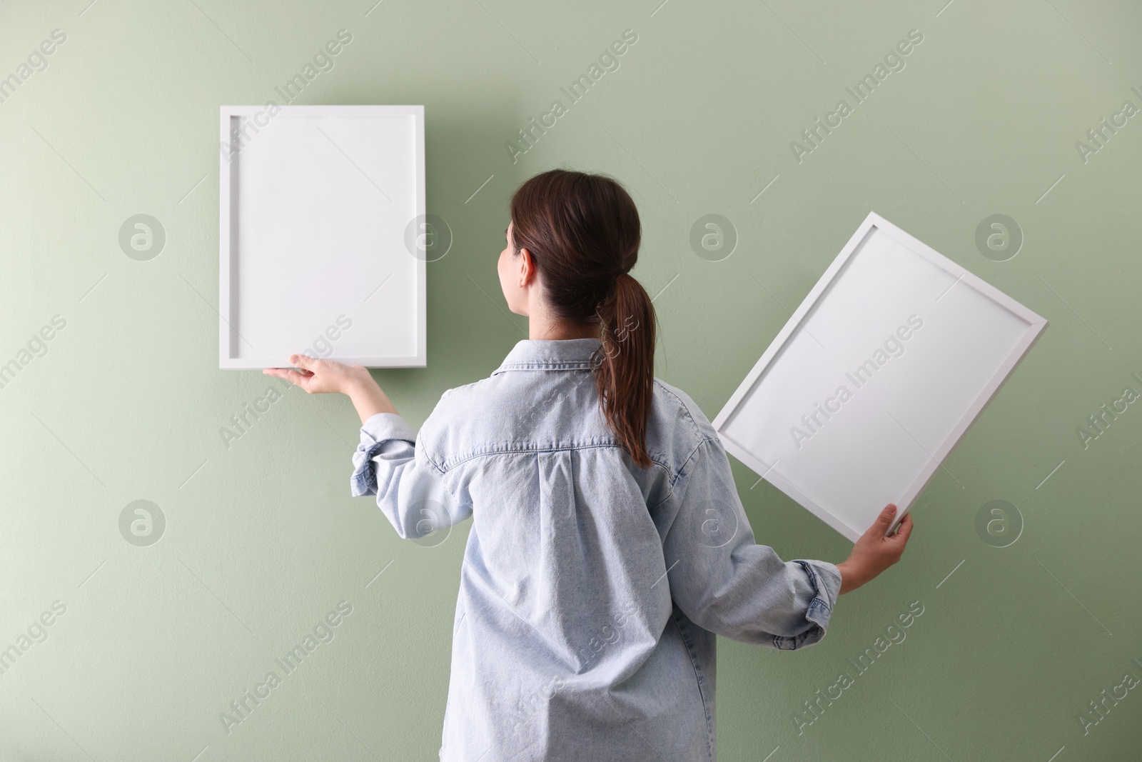 Woman hanging blank frames on green wall, back view Photo of Woman hanging blank frames on green wall, back view